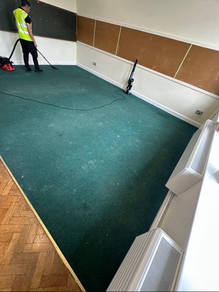 Cleaning specialist in hi-vis vest vacuuming a large green carpet in a commercial or school hall in Dublin