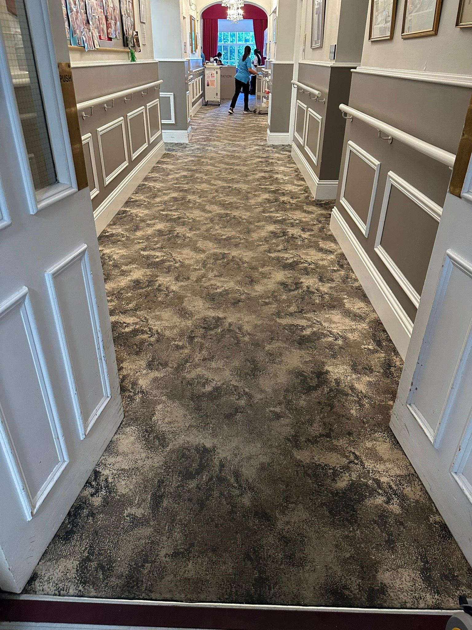 Clean patterned carpet in hotel hallway viewed through open doorway